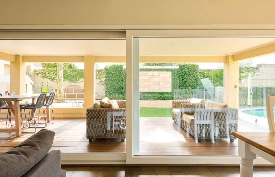 View through a wide white sliding door onto a timber deck with outdoor lounge seating and a garden