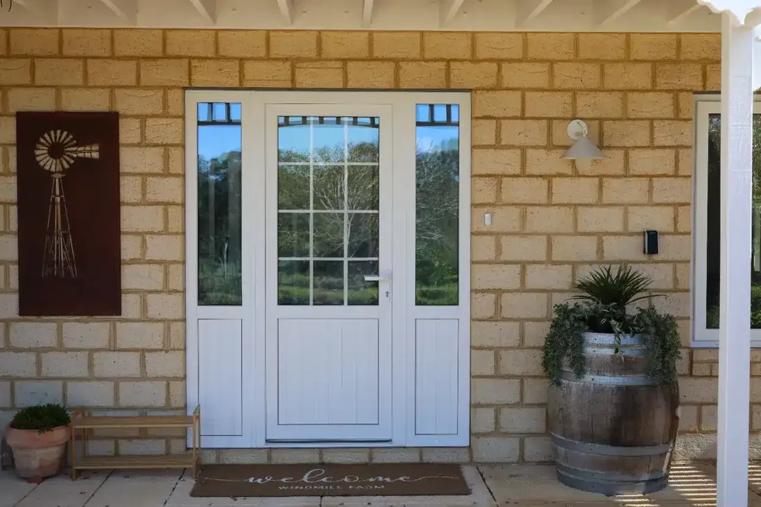 White uPVC entry door with glazed sidelights on a limestone-brick home, beside a wine-barrel planter