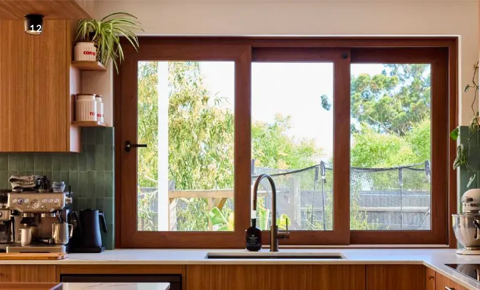 Timber-framed sliding window above a kitchen sink with a green-tiled splashback and garden outlook